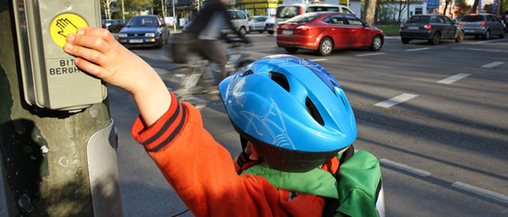 Ein Kind mit Fahrradhelm drückt auf den Knopf an der Fußgängerampel.