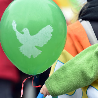 Kinderhand hält Luftballon mit aufgedruckter Friedenstaube in der Hand.