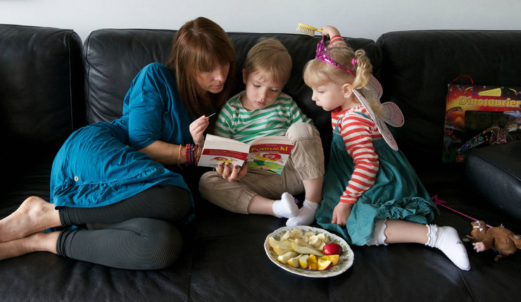 Mutter sitzt mit Kinder auf der Couch und sie lesen ein Buch.