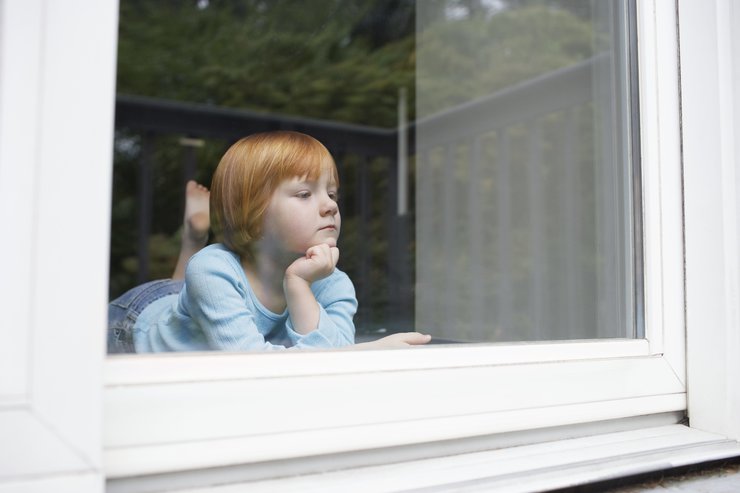 Ein Kind schaut melancholisch durch eine Fensterscheibe