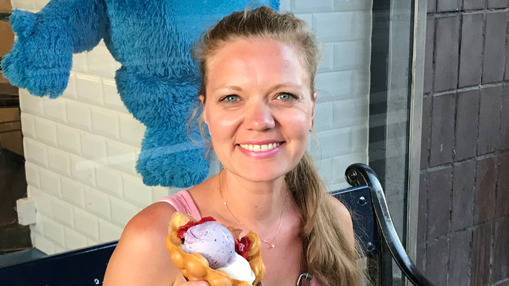 Eine Frau sitzt lächelnd auf einer Bank vor einer bunten Wand und hält ein Eis in der Hand | Bildquelle: Mariana Zech Eine Frau sitzt lächelnd auf einer Bank vor einer bunten Wand und hält ein Eis in der Hand