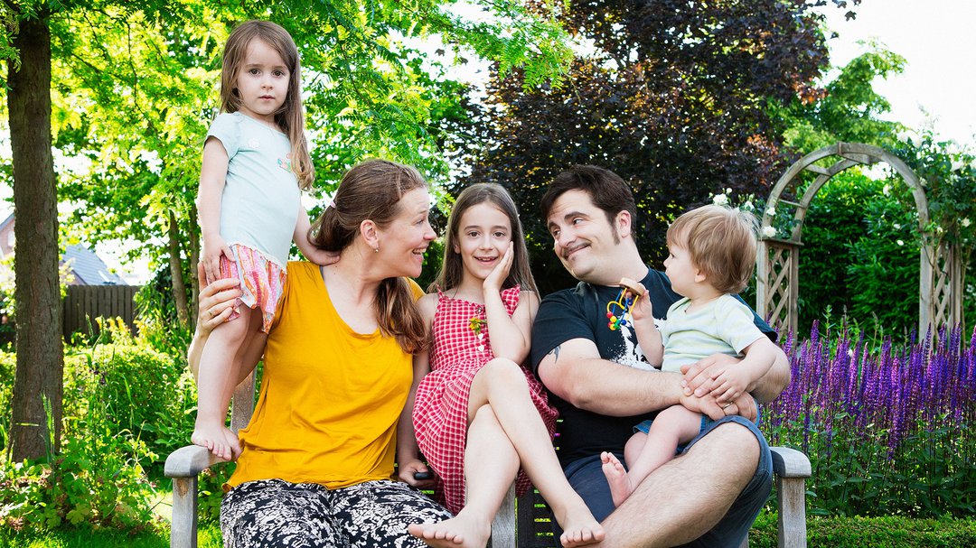 Eine Familie mit drei Kindern sitzt in einem Garten auf der Bank