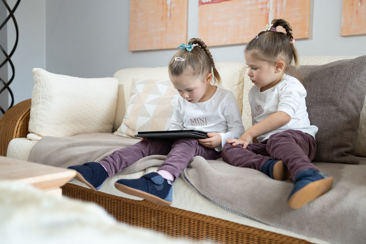 Zwei Mädchen sitzen auf einer Couch, eine davon hat ein Tablet auf ihrem Schoß.