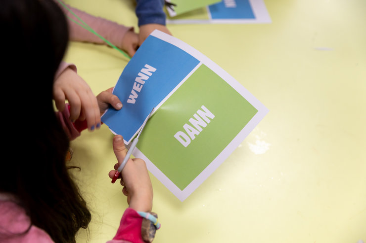 Ein Kind schneidet ein Papier mit den Worten Wenn und Dann auseinander.