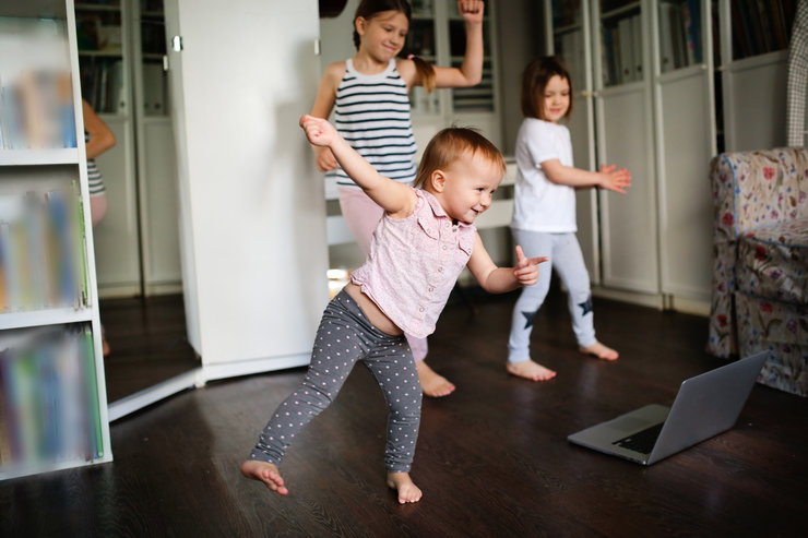 Kinder tanzen im Wohnzimmer vor einem Laptop.