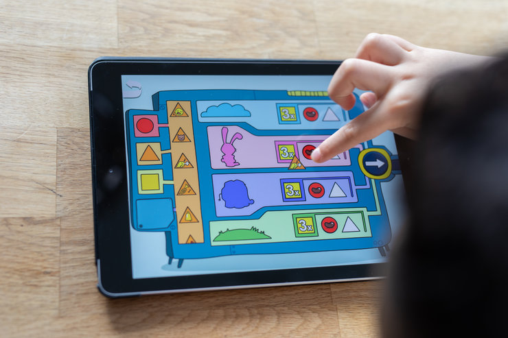 Ein Kind tippt auf ein Tablet, das die Benutzeroberfläche von Programmieren mit dem Elefanten anzeigt.