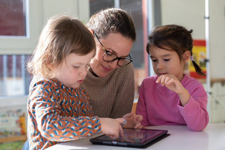 Zwei Kinder mit einer Frau schauen auf ein Tablet