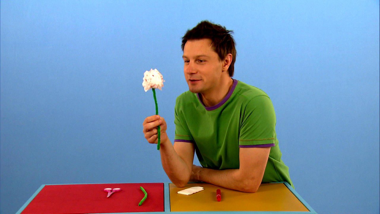 André hält ein Taschentuch-Blume in der Hand, auf der Theke liegen die Bastelutensilien.