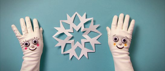 Zwei Hände in weißen Handschuhen, dazwischen eine Papier-Schneeflocke