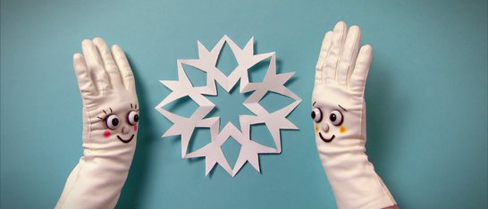 Zwei Hände in weißen Handschuhen, dazwischen eine Papier-Schneeflocke