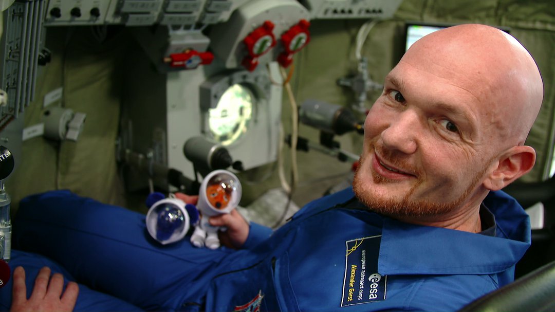 Alexander Gerst in der Raumstation mit Elefant und Maus in Raumanzügen