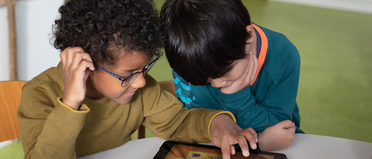 Zwei Kinder am Tisch schauen auf ein Tablet mit der ElefantenApp
