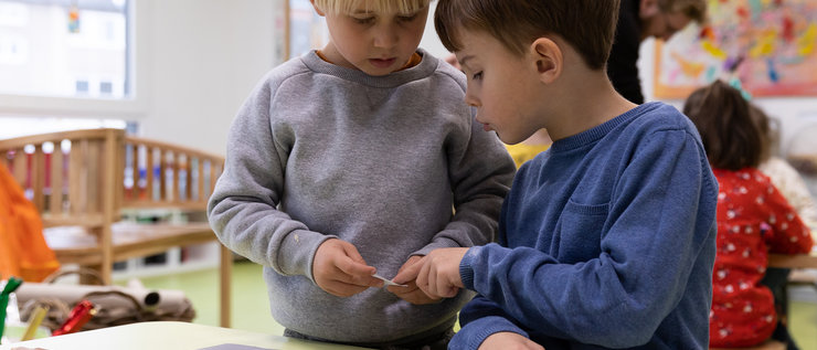 Zwei Kinder am Tisch spielen mit Arbeitsblättern