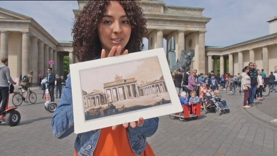 Eine Frau steht vor dem Brandenburger Tor und hält ein Bild hoch