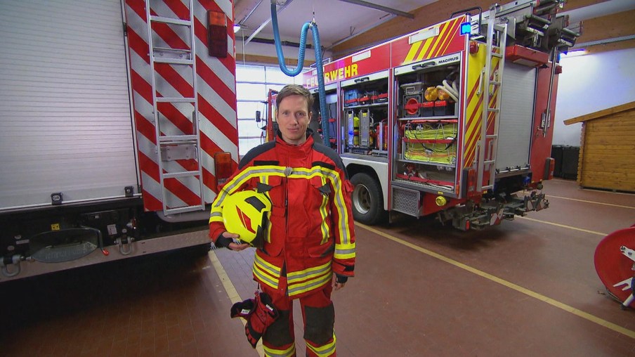 Johannes im Feuerwehranzug umgeben von Feuerwehrwagen in einer Garage