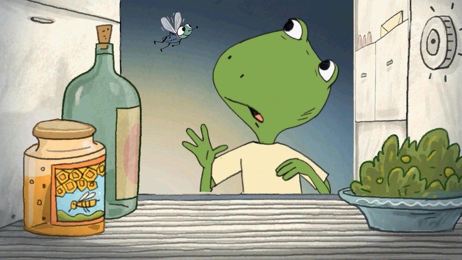 Frosch steht in der Küche vor einem Glas Honig, einer Flasche und einem Teller mit Salat und über ihm fliegt eine Fliege