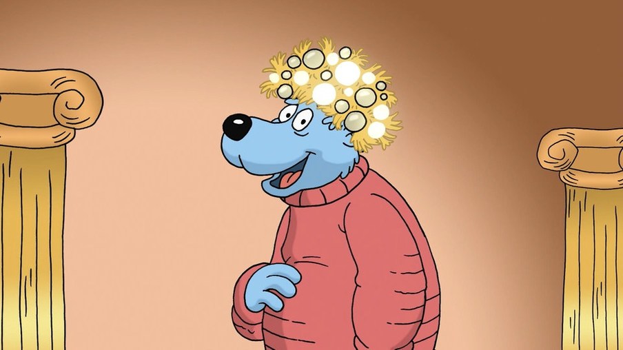 Käpt'n Blaubär steht mit einem roten Pullover bekleidet und einer gefühlten Krone auf dem Kopf vor einer Säule