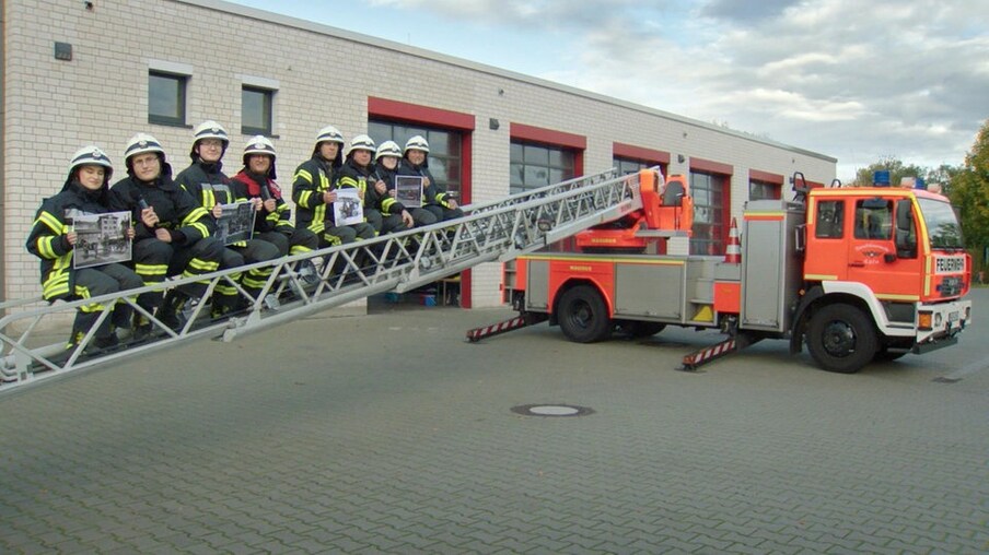 Feuerwehrleute auf Leiter mit Fotos neben einem Feuerwehrwagen