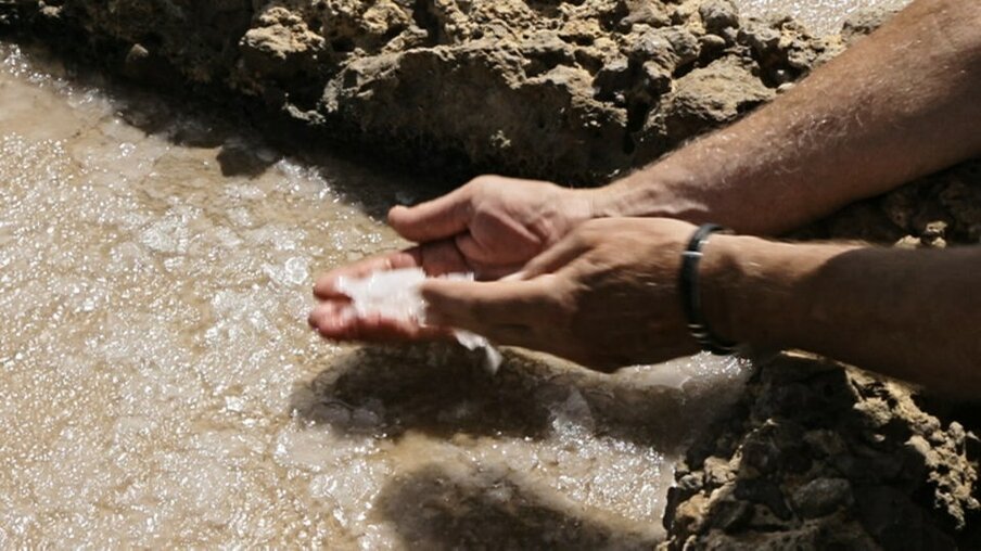 Hände mit Salzkristallen über einem Salzwasserbecken