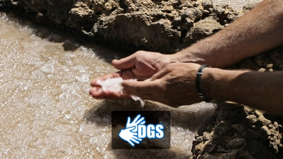 Hände mit Salzkristallen über einem Salzwasserbecken mit DGS-Logo
