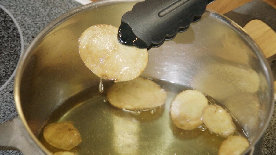 Kartoffelchip auf einer Zange, der aus einem Topf mit Öl genommen wird