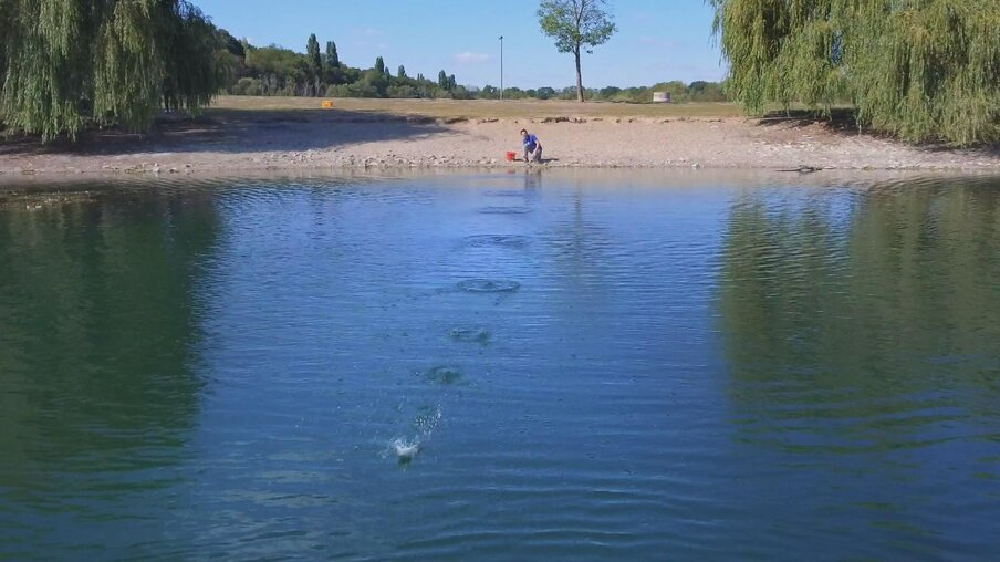 Andrè hockt am Ufer eines Sees und titscht einen Stein