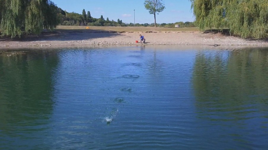 Andrè hockt am Ufer eines Sees und titscht einen Stein