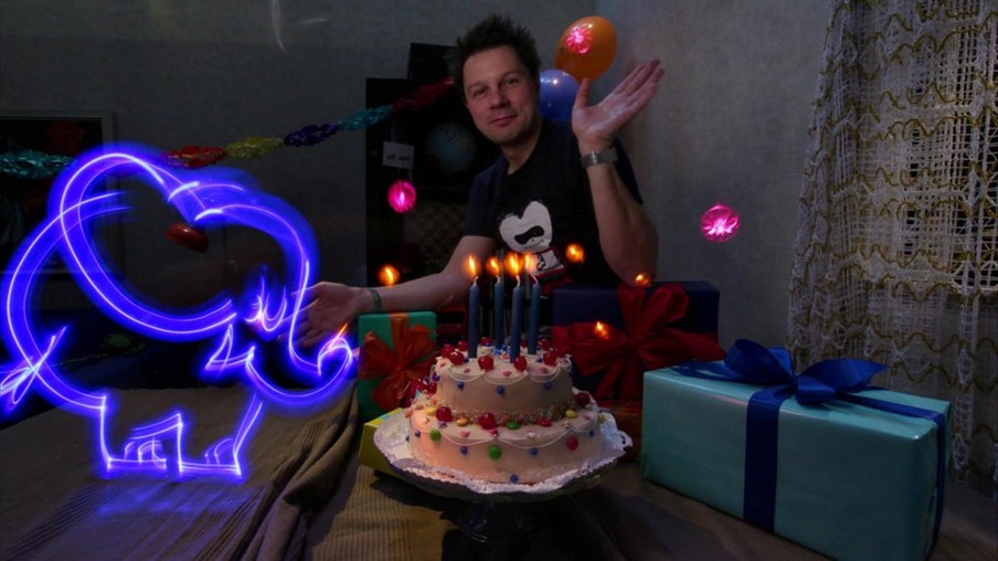 André in einem abgedunkelten Zimmer mit einem Lichtelefanten und einer Torte mit brennenden Kerzen
