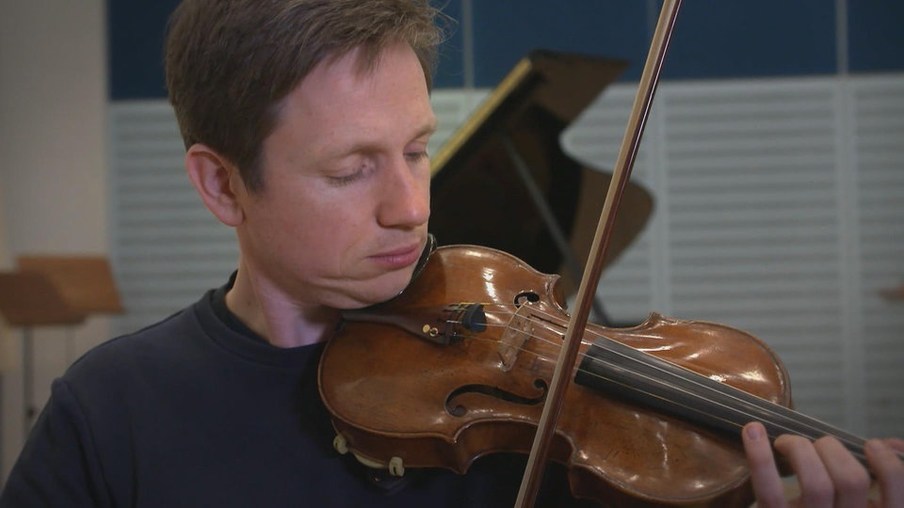 Johannes hält einen Bogen und einer Geige spielbereit in der Hand