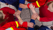 Menschen in roter Warnkleidung bilden mit ihren Armen einen Kreis.